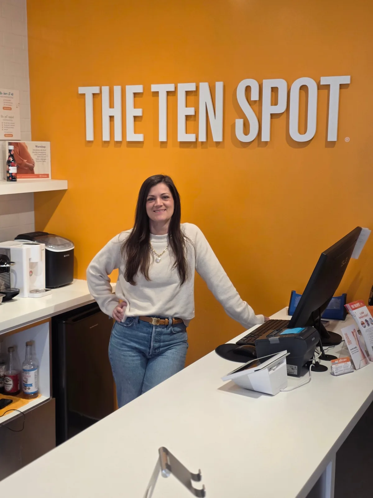 Jon's wife at the front desk of The Ten Spot, the downtown Guelph business the couple owns, beneath the studio logo.