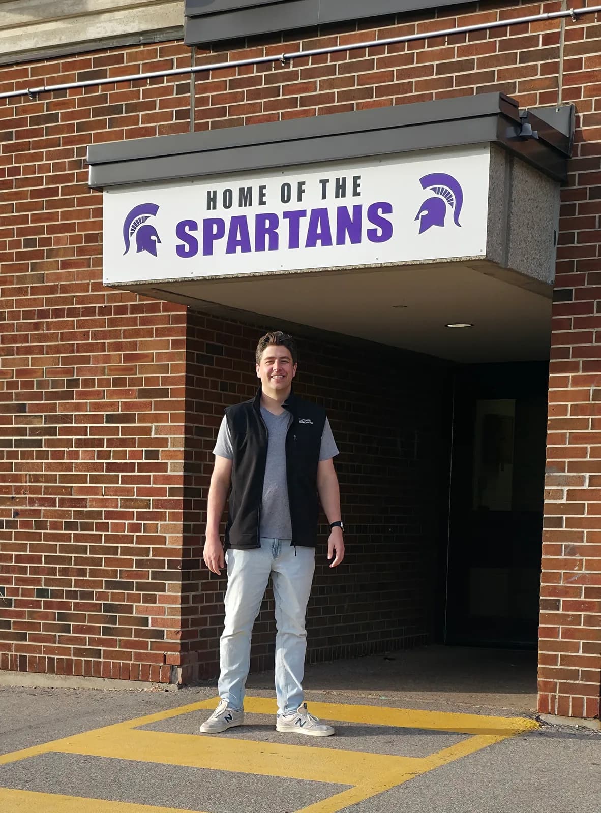 Jon Christensen standing beneath the Home of the Spartans sign at the entrance to Centennial CVI, his old high school in Ward 5.